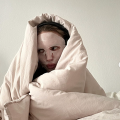 A woman wearing a face mask wrapped in a blanket in bed 