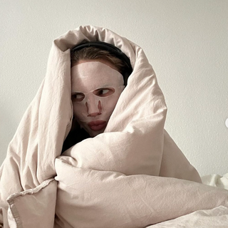 A woman wearing a face mask wrapped in a blanket in bed 