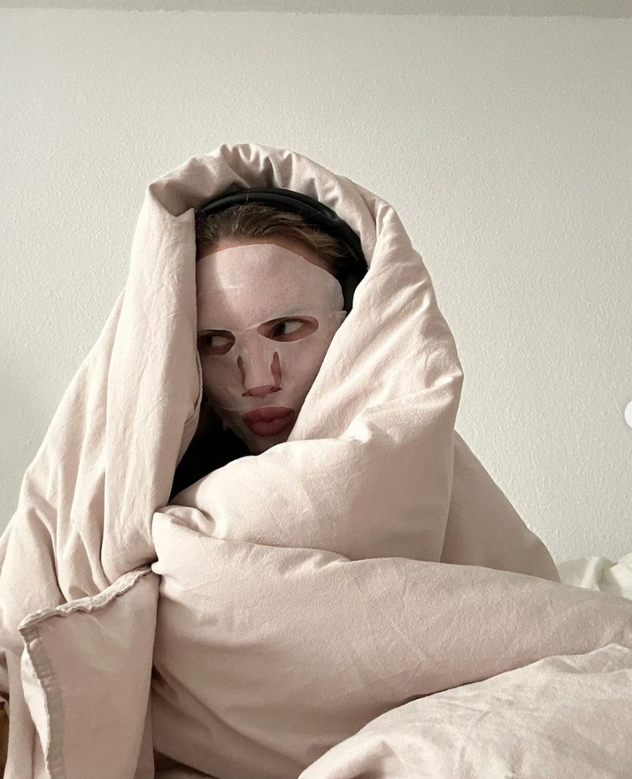 A woman wearing a face mask wrapped in a blanket in bed 