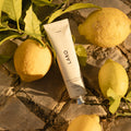 Naturally Whitening Toothpaste tube for Laro with hexagonal aluminium cap, surrounded by lemons and lemon tree branches in golden hour light on a stone surface.